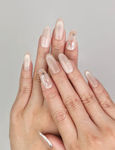 Hand wearing Naillover Shimmering Beige handmade press on nails with luminous cat eye effect and chic gold foil accents.